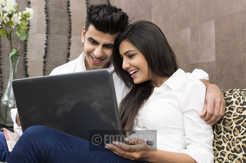 couple sitting on couch browsing on laptop