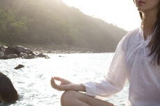 young woman meditating alongside river