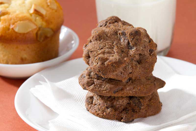 close up of chocolate cookies with muffins and milk