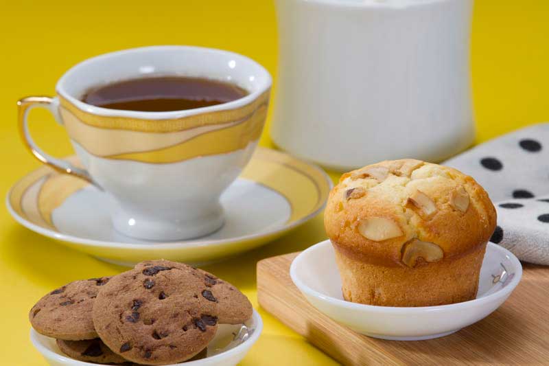 tea,muffins and cookies against a yellow background