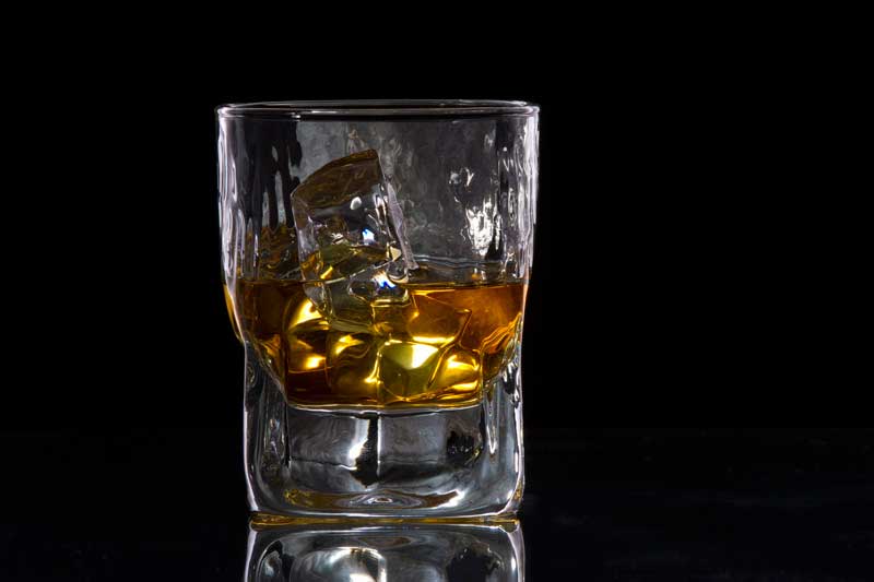 a glass of scotch with ice cubes against dark background 