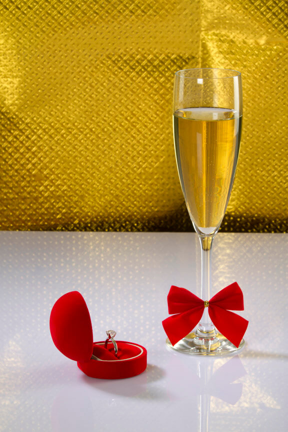 close shot of a glass of wine with wedding ring on golden background