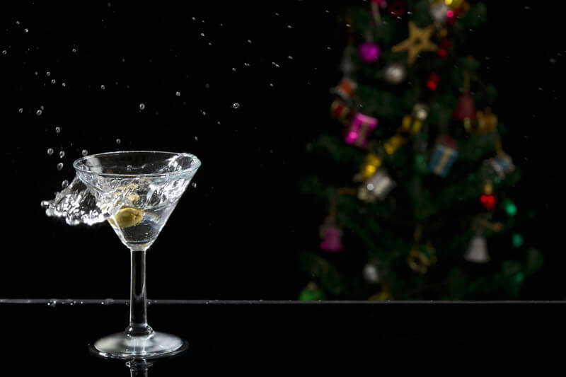 close up shot of martini drink with splash and christmas tree in the b