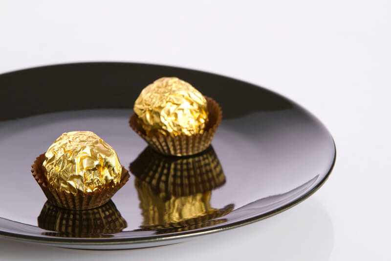 two chocolate nuts placed on a black plate against white background