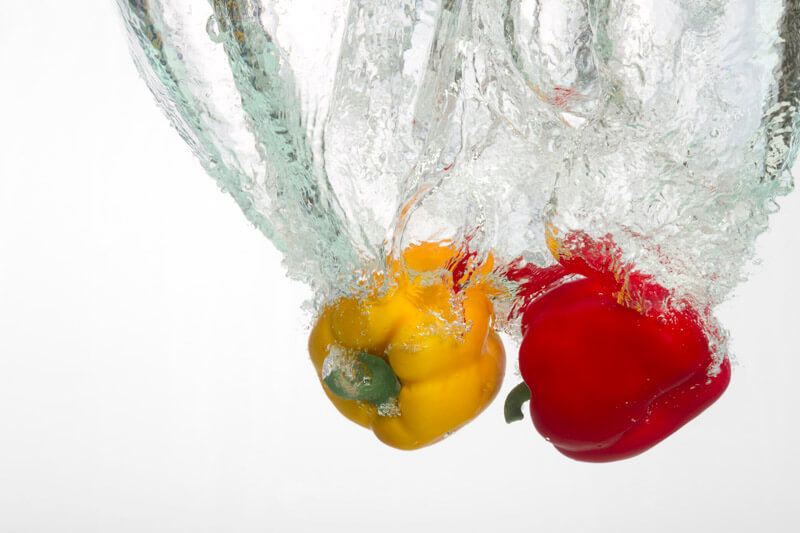 red and yellow capsicums in water against white background