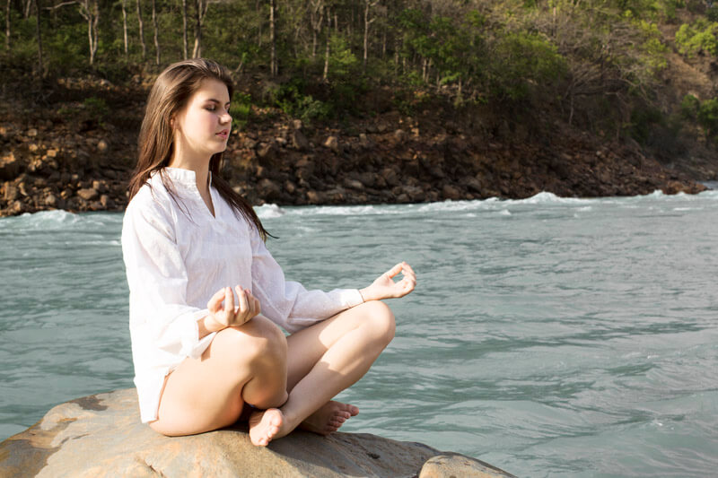 woman meditating on a rock along riverside