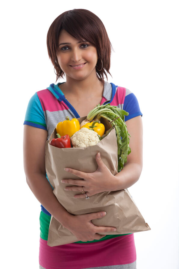 young housewife holding bag full of vegetables with both hands 