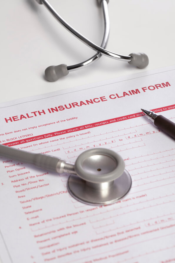 insurance claim form lying on table with a pen and stethoscope 