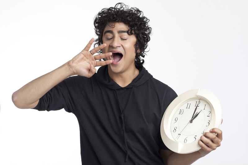 male teenager yawning with a clock