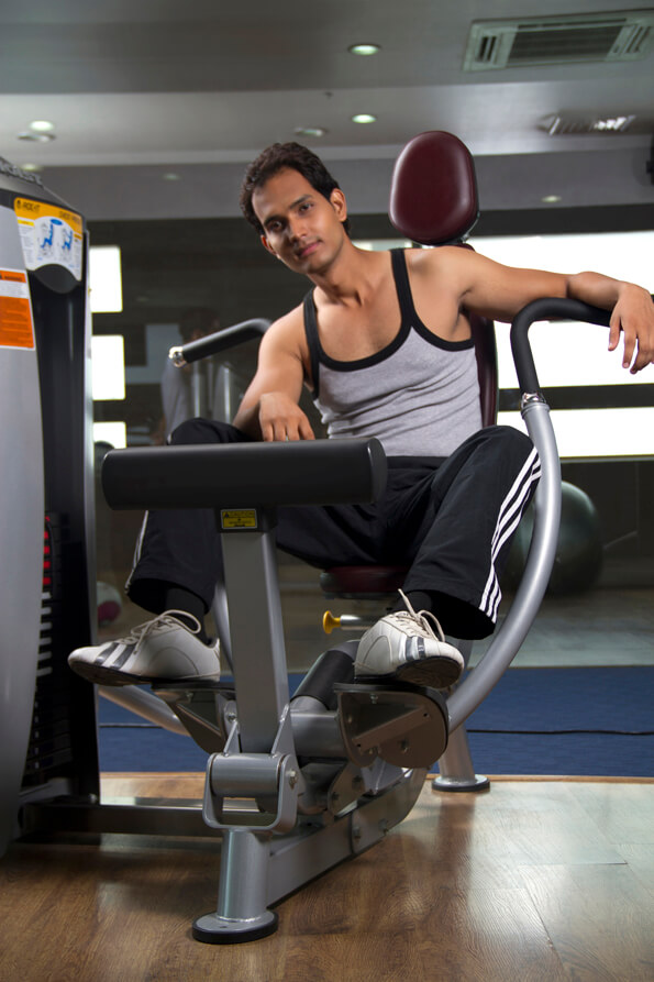 man posing with leg exercising machine at the gym
