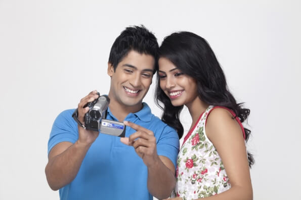 couple smiling while recording something with video camera 