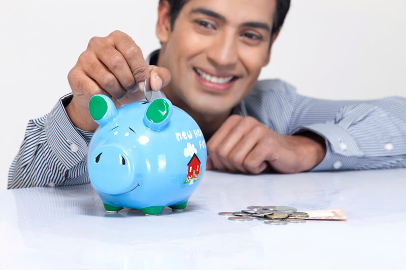 young man dropping a coin in a piggy bank
