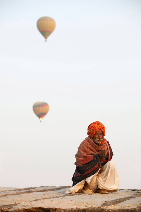 rural man sitting with hot air balloons in background 