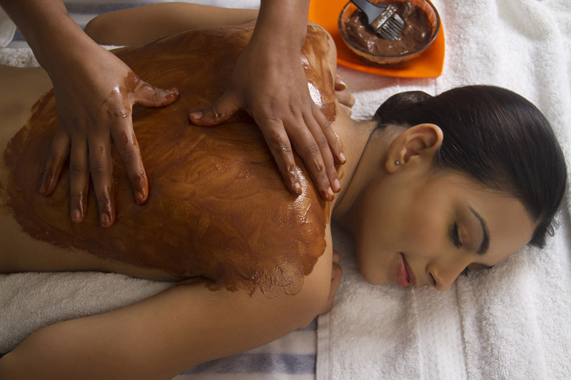therapist applying ayurvedic solution at the back of the lady 
