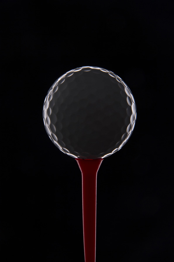 golf ball on golf tee against dark background 