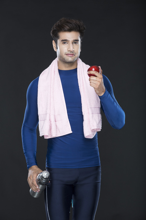 healthy young guy in gym wear holding an apple and sipper 