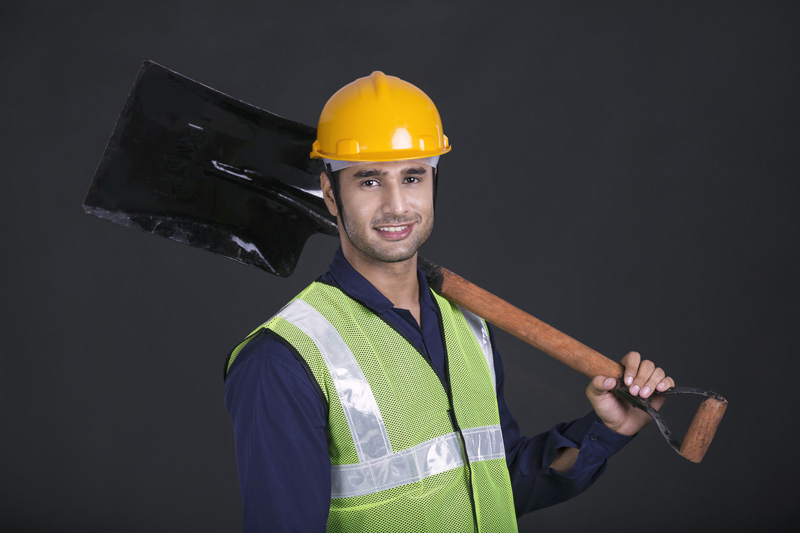man carrying shovel on shoulder against dark background