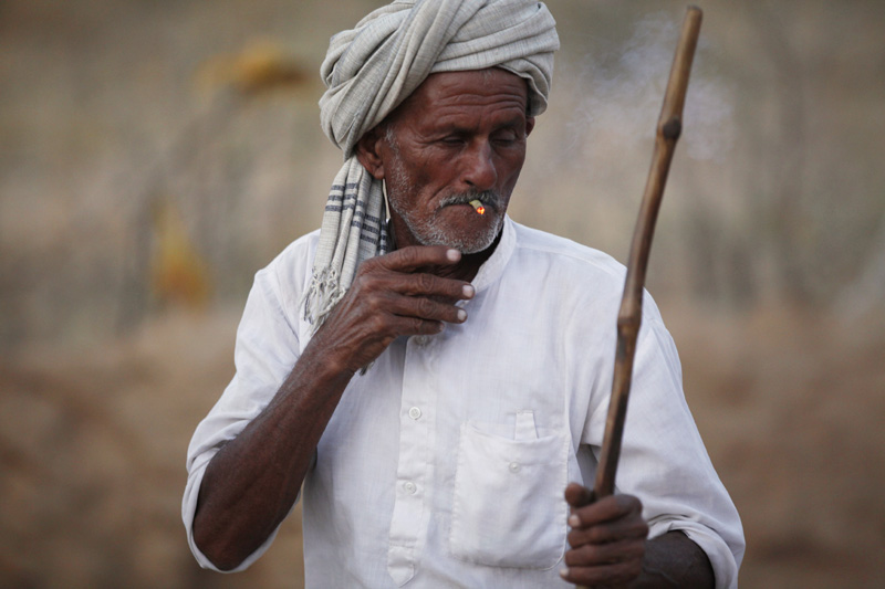 villager on field smoking beedi while holding bamboo