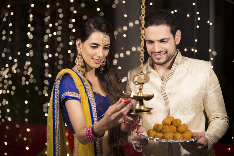 couple holding ladoos and lighting lamp