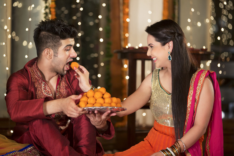 couple celebrating diwali by feeding each other ladoos 