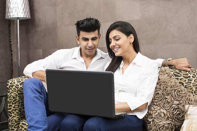 couple on couch browsing in laptop and smiling  