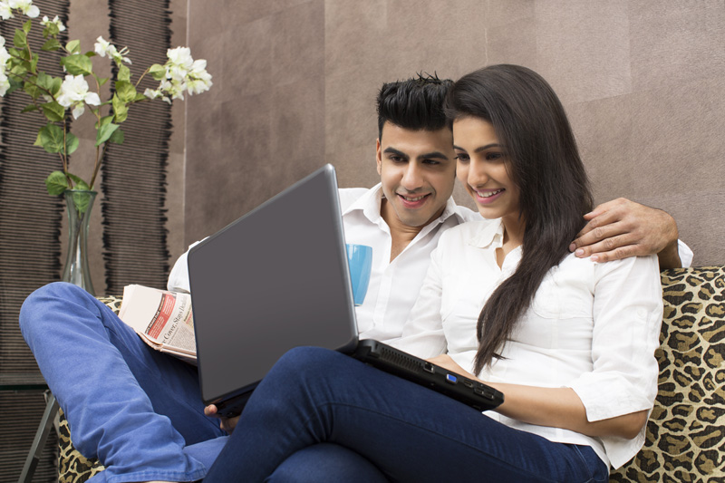 couple smiling on couch while browsing in laptop