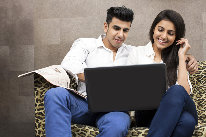couple on couch browsing in laptop and smiling 