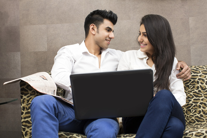 couple with laptop smiling while looking at each other
