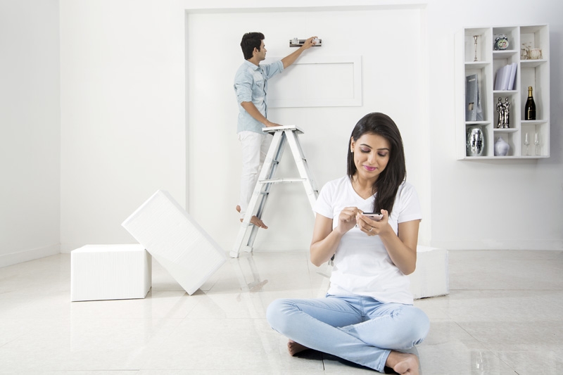 husband decorating home while wife messaging on mobile