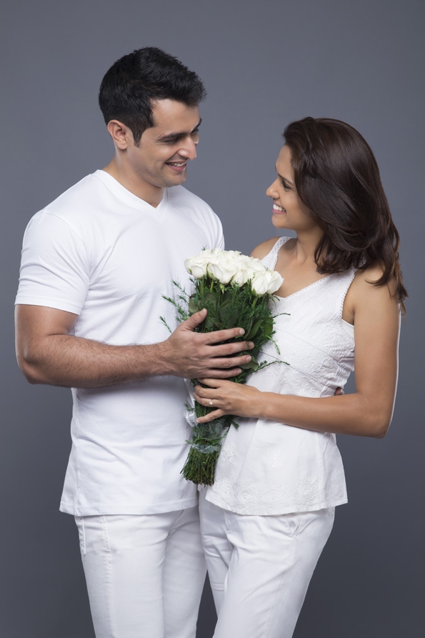 portrait of young couple in love with flowers posing against grey