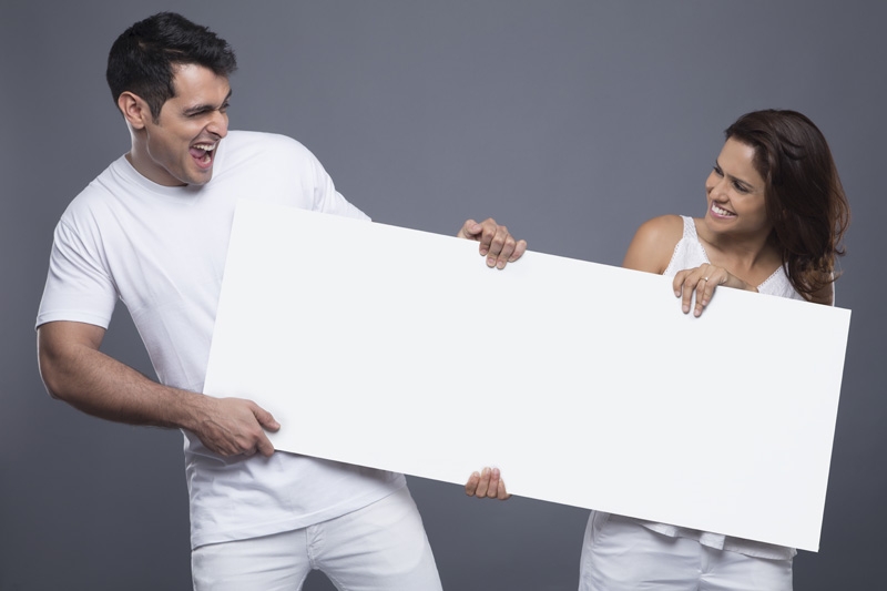 smiling young couple holding and looking at the blank board