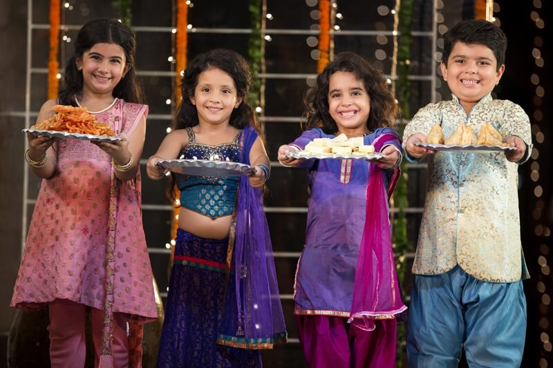 group of kids standing and offering sweets on diwali