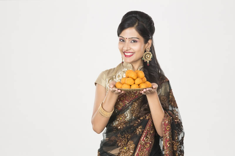 woman in saree with a plate of ladoos 