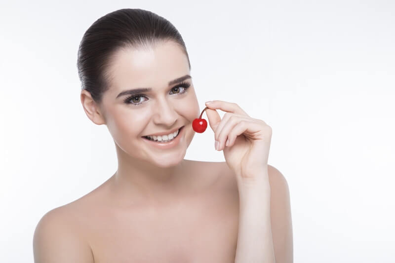 girl smiling and holding cherry while posing
