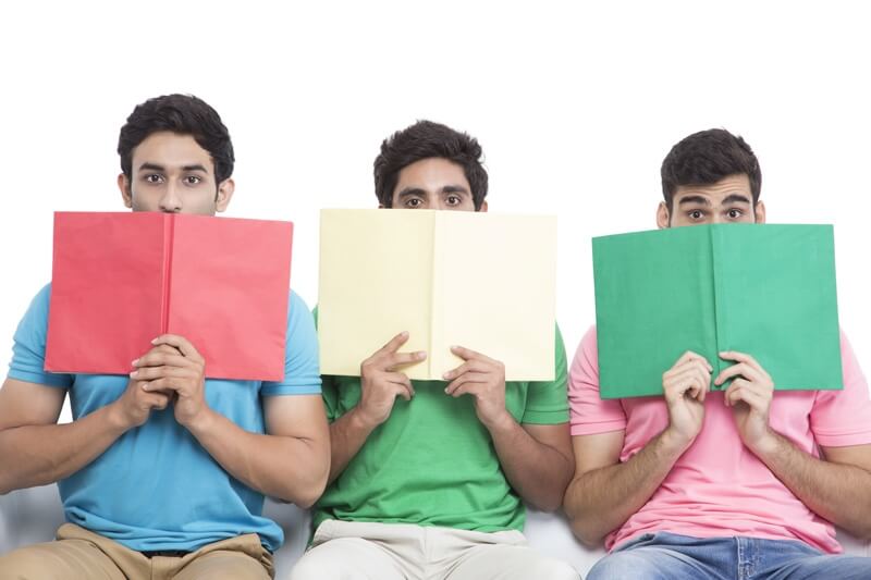 three friends sitting in a row hiding faces with books