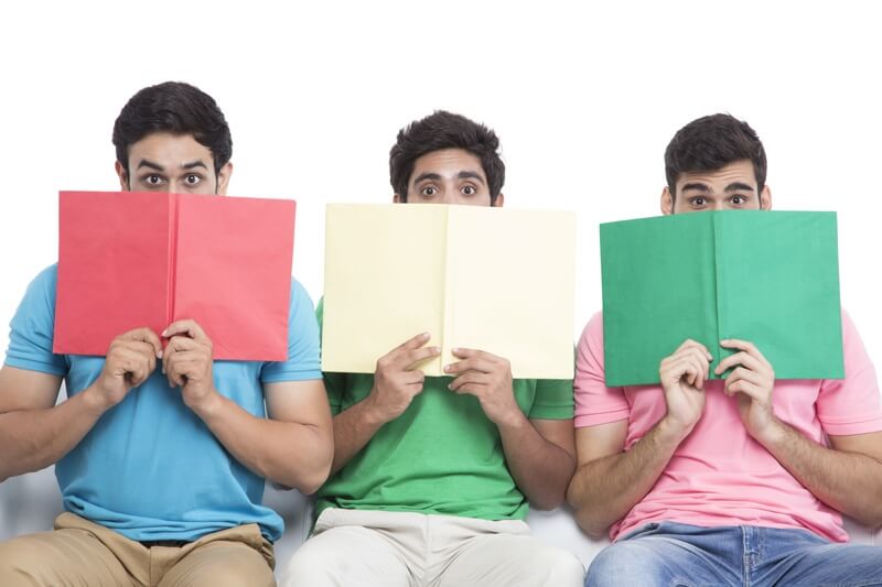 three friends sitting in a row hiding faces with books