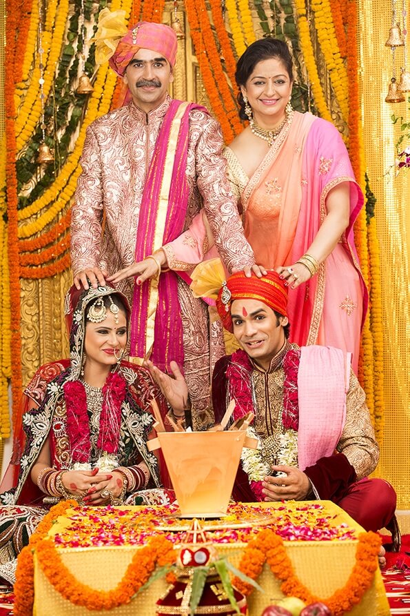 indian bride and groom sitting with parents at mandap