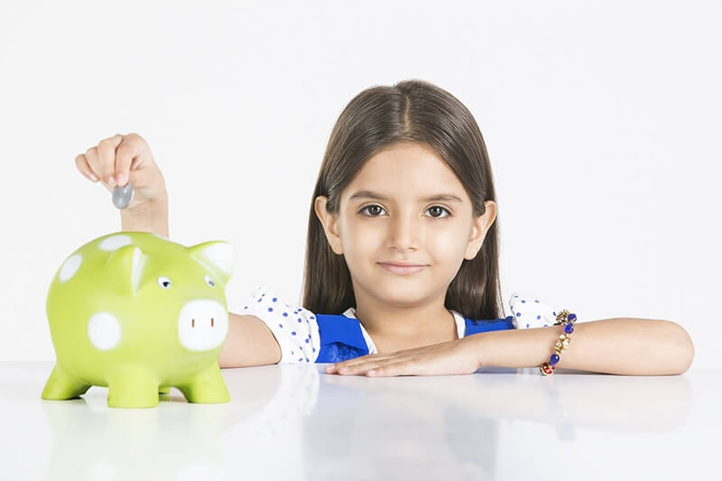young girl depositing money in piggy bank