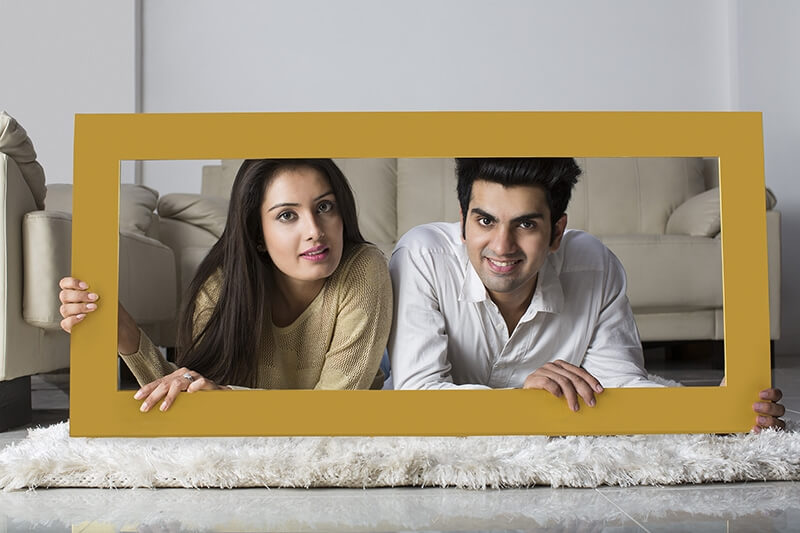 young couple posing with wooden frame at home