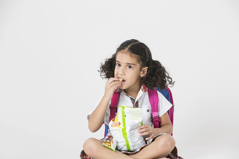 little girl in school uniform eating chips