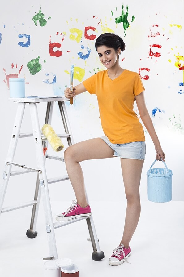 girl posing with paint brush with hand prints in the background