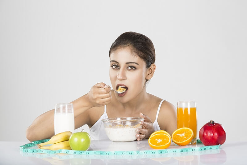 Young woman eating conflex in bowl with healthy fruits milk & juice